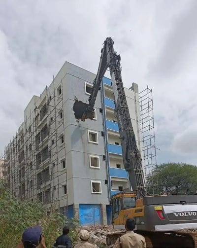 A HYDRA excavator demolishing a building in Hyderabad, showing the brutal truth of what can happen when **buying an apartment** built on encroached land.